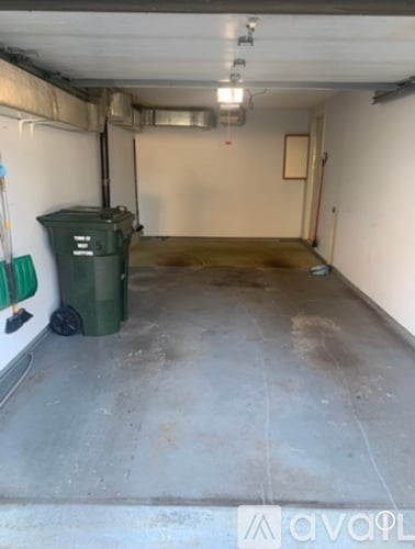 A dirty garage with a green trash can and a white wall.