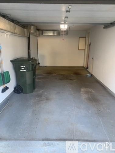 A dirty garage with a green trash can and a white wall.