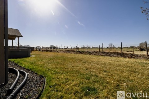 A sunny day in a field with a fence and a building in the background.
