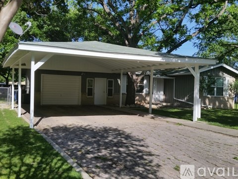 A covered garage with a brick driveway in front.
