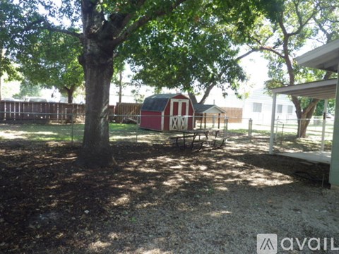 A red barn with a white door is surrounded by a fence and trees.