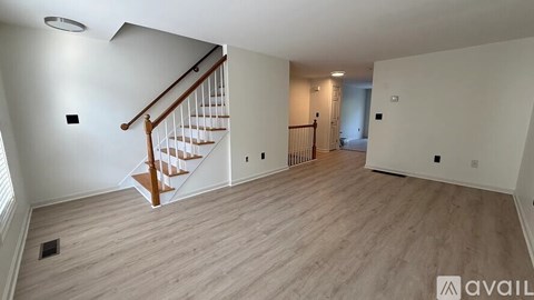 A spacious room with wooden flooring and a staircase.