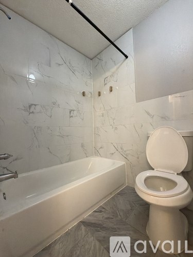 A bathroom with a white toilet and a white bathtub with marble wall tiles.
