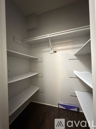 A small, empty walk-in closet with white shelves and a wooden floor.