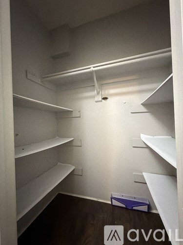 A small, empty walk-in closet with white shelves and a wooden floor.