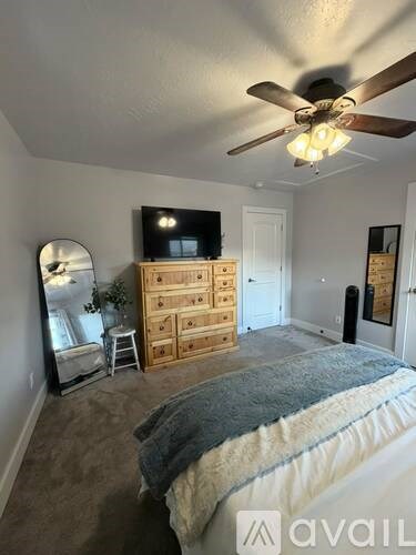 A bedroom with a bed, dresser, mirror, and ceiling fan.
