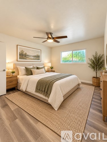 A bedroom with a bed, a ceiling fan, and a painting on the wall.