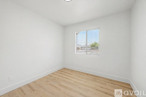A room with wooden flooring and a window showing a view of a building and trees outside.