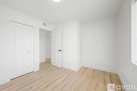 A room with white walls and wooden flooring, with a door on the left and a smaller door on the right.