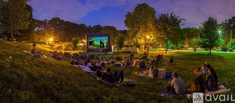 A group of people are sitting on the grass watching a movie in a park.