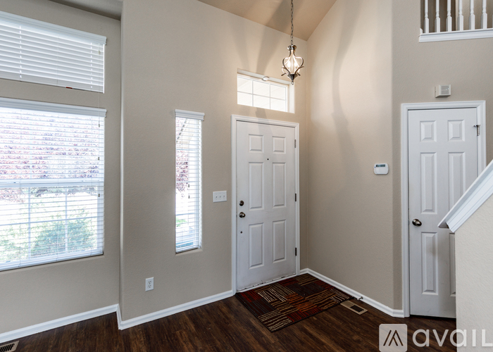 A room with a white door, a window with blinds, and a chandelier.