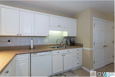A kitchen with white cabinets and a countertop with a sink and dishwasher.