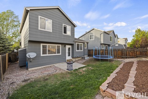 A house with a grey exterior and a blue swing set in the backyard.