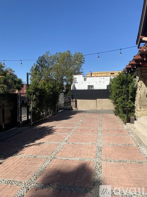 A brick pathway leads through a courtyard with a white building in the background.