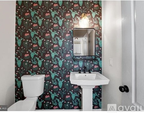 A bathroom with a white toilet, sink, and a wallpapered wall.