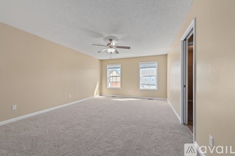 A spacious room with a ceiling fan and two windows.