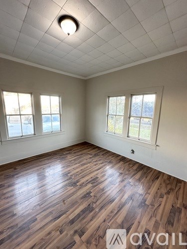 A room with wooden flooring and two windows.
