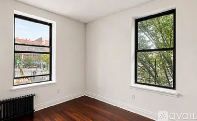 A room with two windows, one of which has a view of a street with cars and buildings.