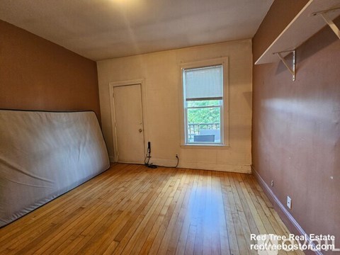 A room with wooden floors and a window with a view of trees.