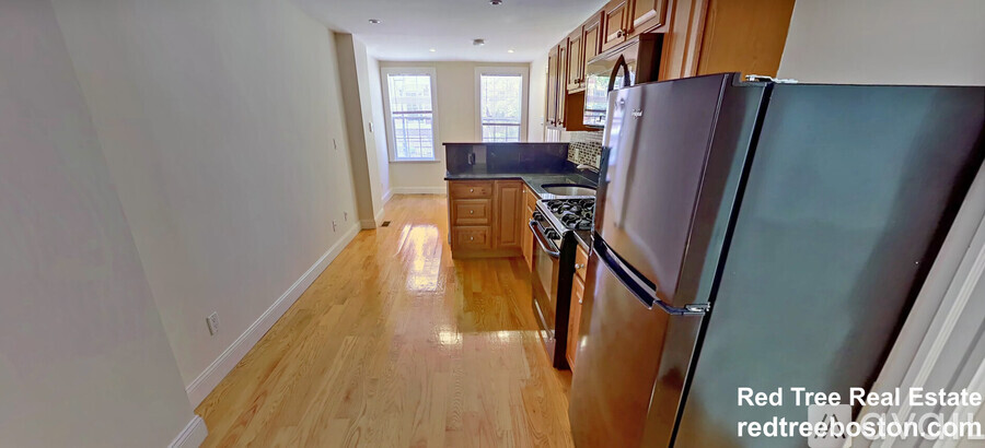 A kitchen with a refrigerator and wooden floors.