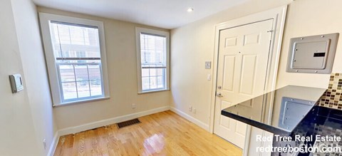 A room with a wooden floor, a white door, and a window with blinds.