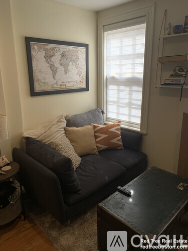 A living room with a grey couch and a world map on the wall.