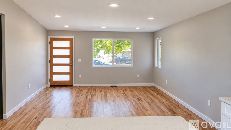 A room with wooden floors and a window showing trees and a car outside.