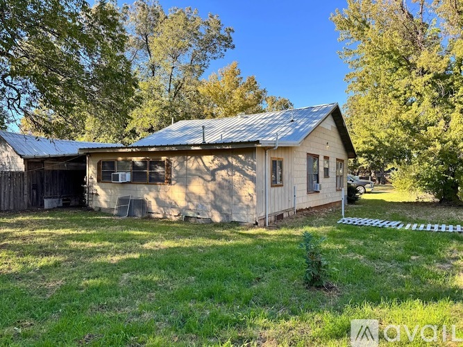 A small house with a metal roof is surrounded by trees.