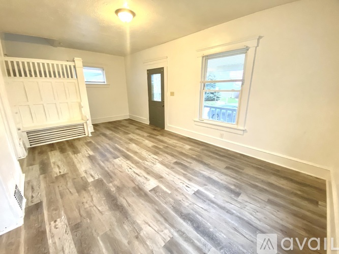A room with wooden flooring and a window showing a view of trees and a building.