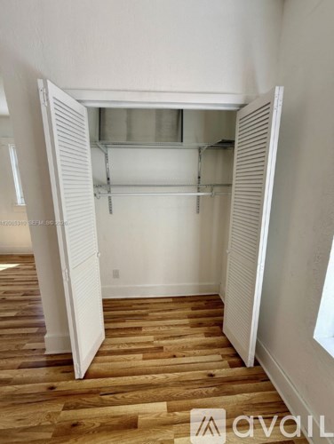 A room with a white wall and wooden flooring with a white closet open.