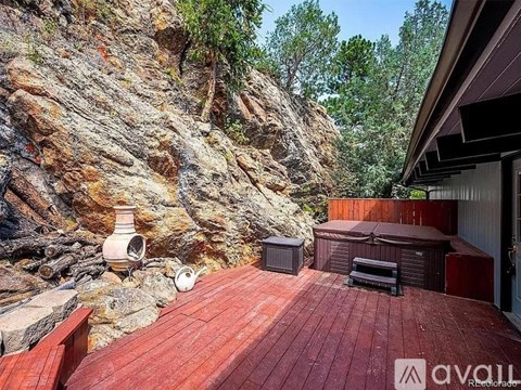 A wooden deck with a hot tub and a stone wall in the background.