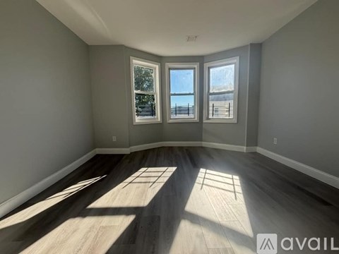 A room with wooden floors and three windows letting in sunlight.