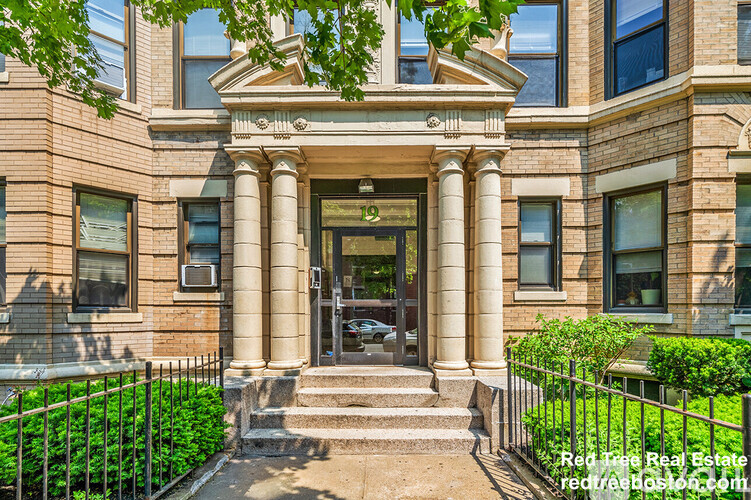 A red brick building with a central entrance and steps leading up to it.