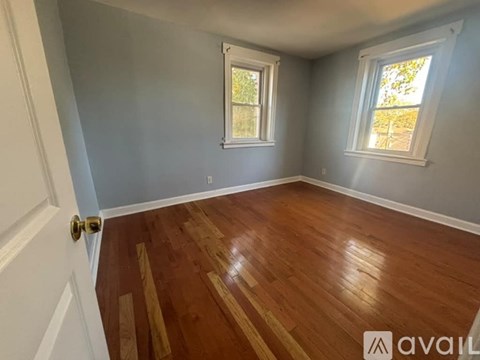 A room with wooden flooring and two windows.