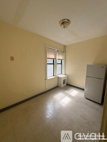 A room with a window, a fridge, and a radiator.