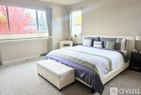 A bedroom with a large bed and a window with red trees outside.