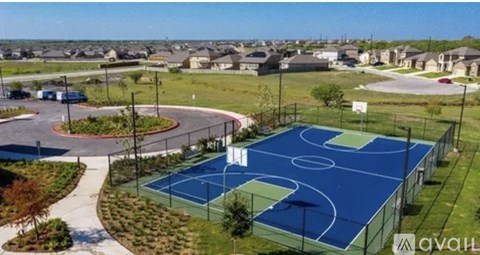 A basketball court is surrounded by a fence and a grassy area with trees.