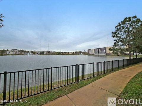 A view of a lake with a fence and buildings in the background.