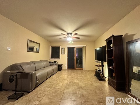 A living room with a couch, a ceiling fan, and a television.
