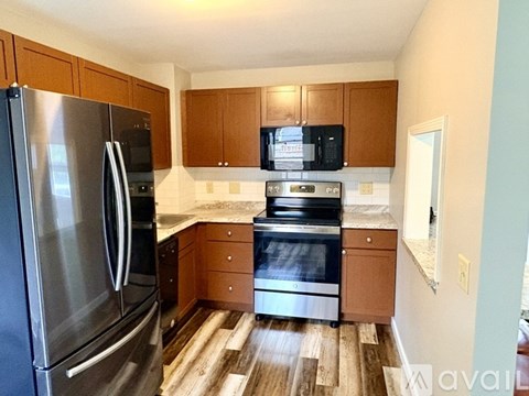 A kitchen with a stainless steel refrigerator and oven, wooden cabinets, and a wooden floor.