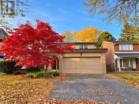A red maple tree in front of a house with a garage.