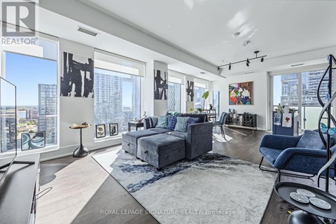 A spacious living room with a grey sofa set and a large window overlooking the city.