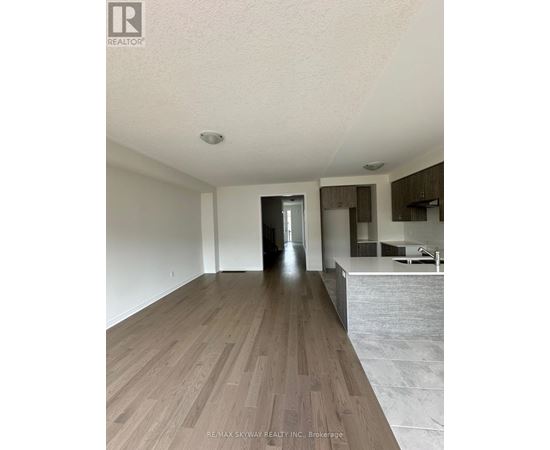 A spacious room with wooden flooring and a kitchen area in the background.
