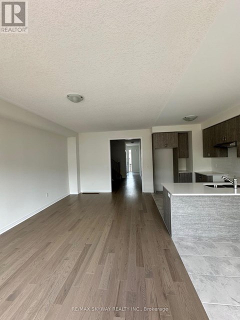 A spacious room with wooden flooring and a kitchen area in the background.