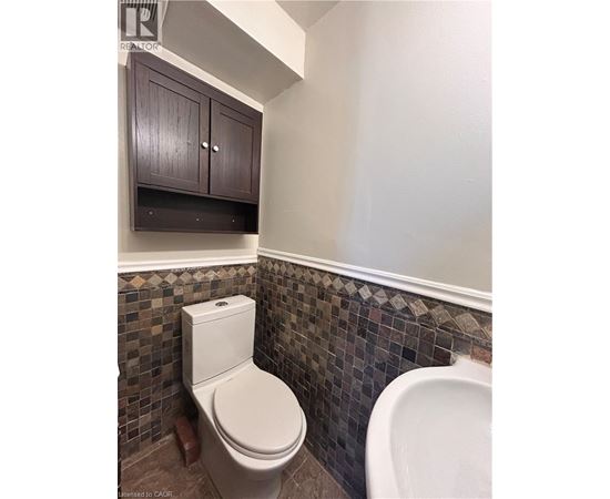 A white toilet in a bathroom with brown cabinets and a tiled wall.