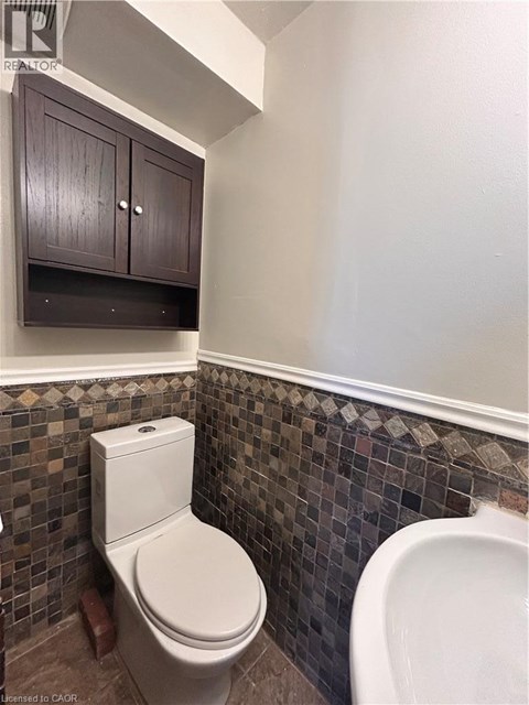 A white toilet in a bathroom with brown cabinets and a tiled wall.