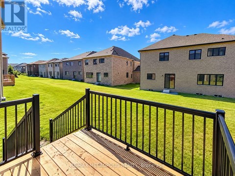 A balcony with a black railing overlooks a grassy area and a row of houses.