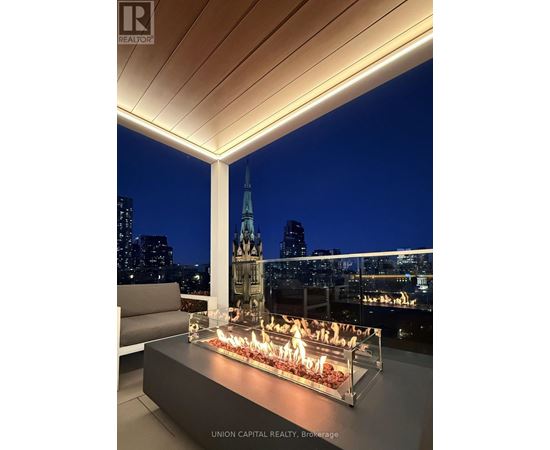 A modern outdoor seating area with a fire pit and a view of the city skyline at night.