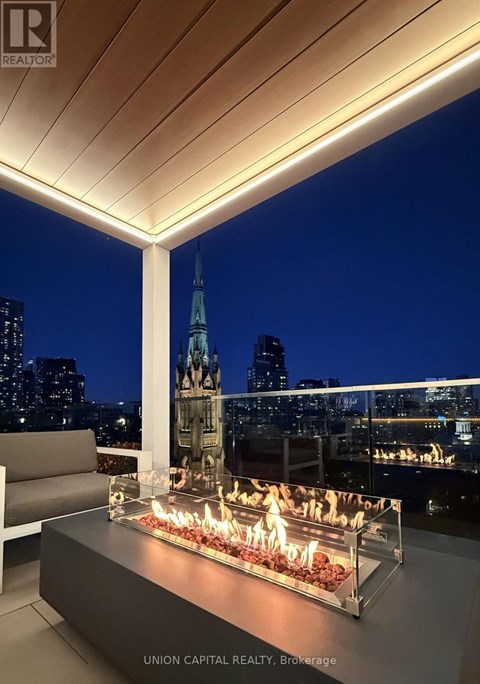 A modern outdoor seating area with a fire pit and a view of the city skyline at night.