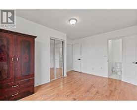 A room with a wooden floor and white walls, with a red cabinet on the left and a toilet in the distance.